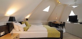 Doppelbett, TV und Tisch mit Stühlen unter der Dachschräge der Turmsuite in Michels Wohlfühlhotel, Rheinland-Pfalz, Vulkan-Eifel, Schalkenmehren